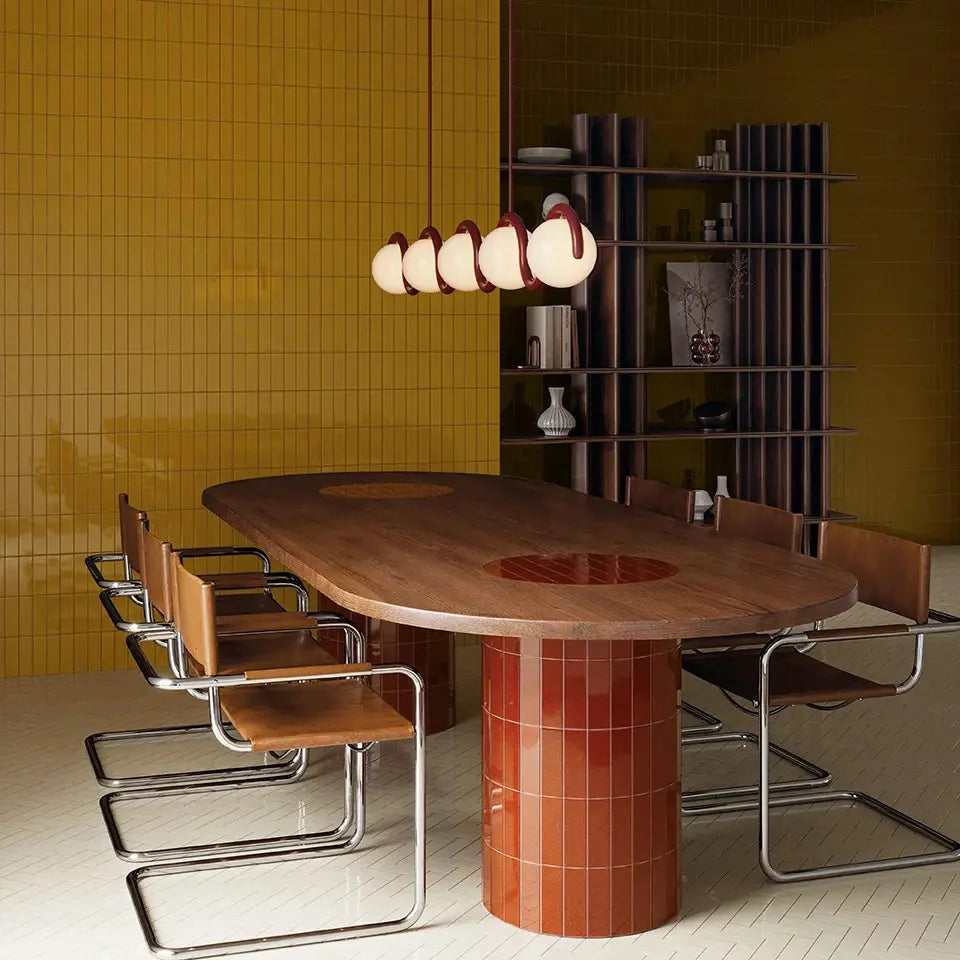 Micare Ambar Dark Gloss 50x150mm mustard yellow wall tiles in a styled dining room with a tiled pedestal table and leather cantilever chairs.