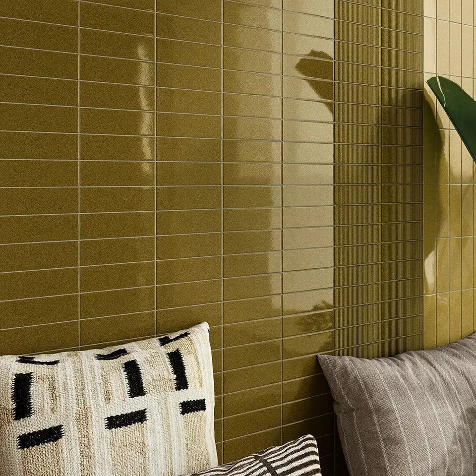 Micare Canale Alpi Dark Gloss 50x150mm olive-green glossy stacked tiles covering a living room feature wall styled with patterned and grey cushions.