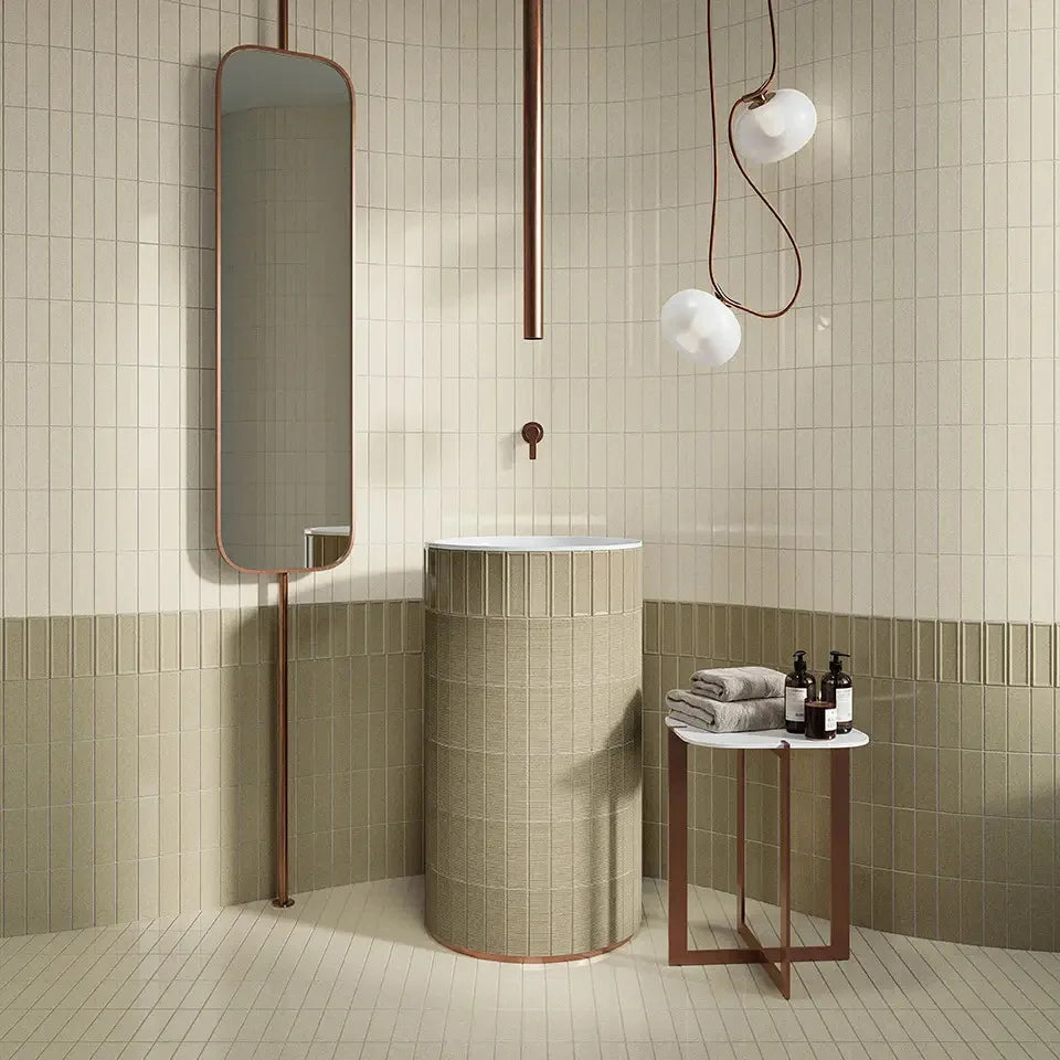 Micare Canale Linen Dark Gloss 50x150mm tiles covering a two-tone bathroom wall and cylindrical pedestal basin, styled with copper fixtures and globe pendant lights.