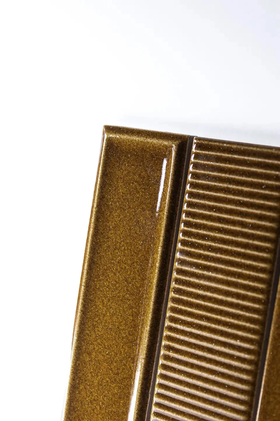 Close-up of Micare Rim Ambar Dark Gloss 50x150mm tiles showing a smooth border tile alongside a ribbed textured tile in a rich amber gloss finish.