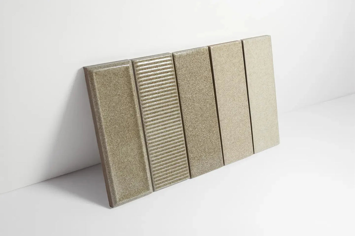 Pack shot of Micare Rim Linen Dark Gloss 50x150mm tiles showing four vertical samples with smooth, ribbed, and matte finishes in warm greige tones.
