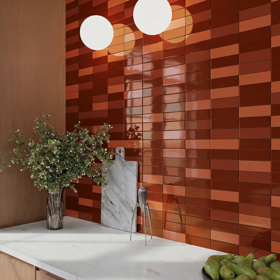 Micare Saffron Dark Gloss 50x150mm tiles installed as a rich terracotta kitchen splashback with white marble countertop, globe pendant lights, and decorative greenery.