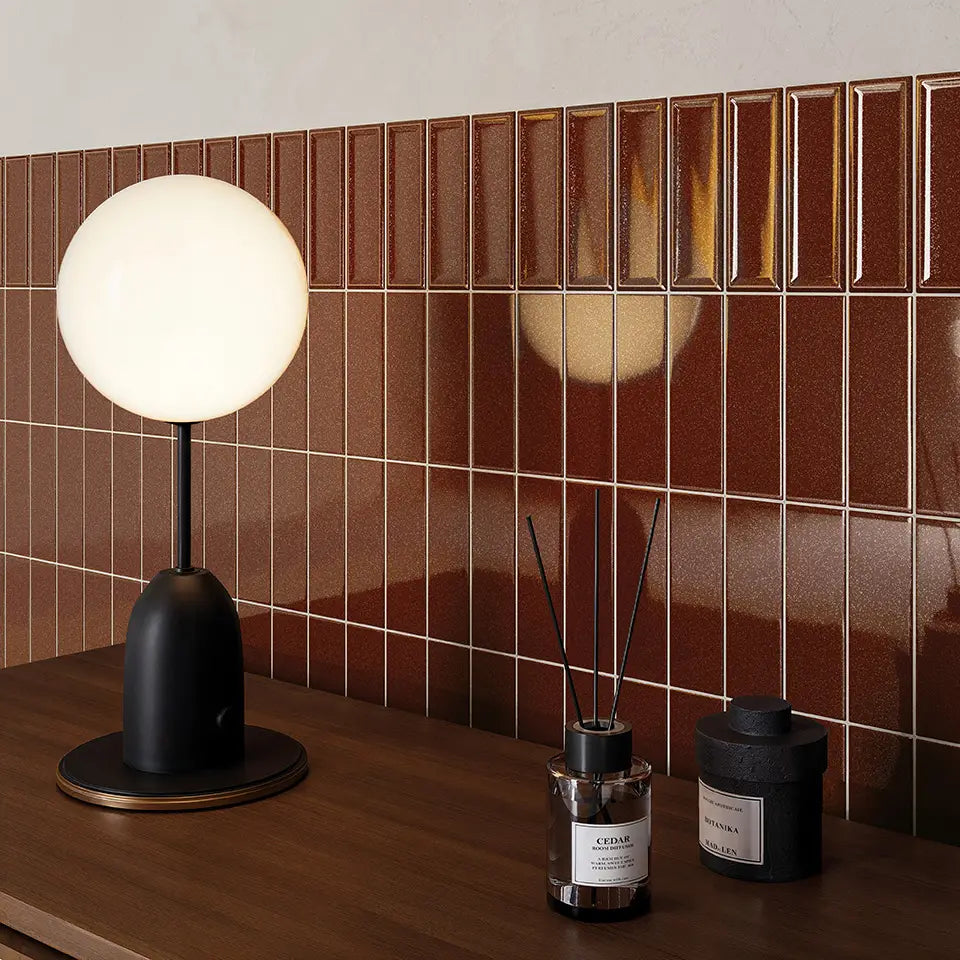 Micare Saffron Dark Gloss 50x150mm tiles installed as a rich brown vertical stack-bond feature wall behind a wooden vanity styled with a globe table lamp and reed diffuser.