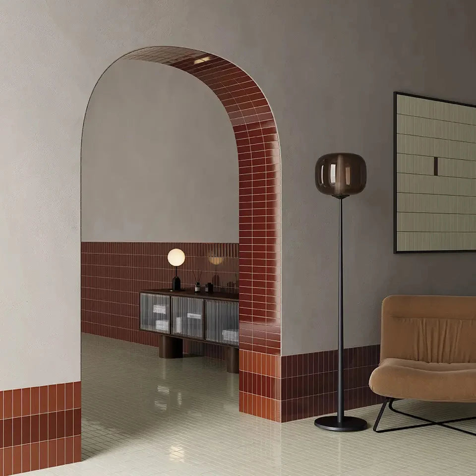 Micare Saffron Light Gloss 50x150mm tiles cladding a bold terracotta arched doorway and wainscoting in a contemporary living room with a floor lamp and lounge chair.