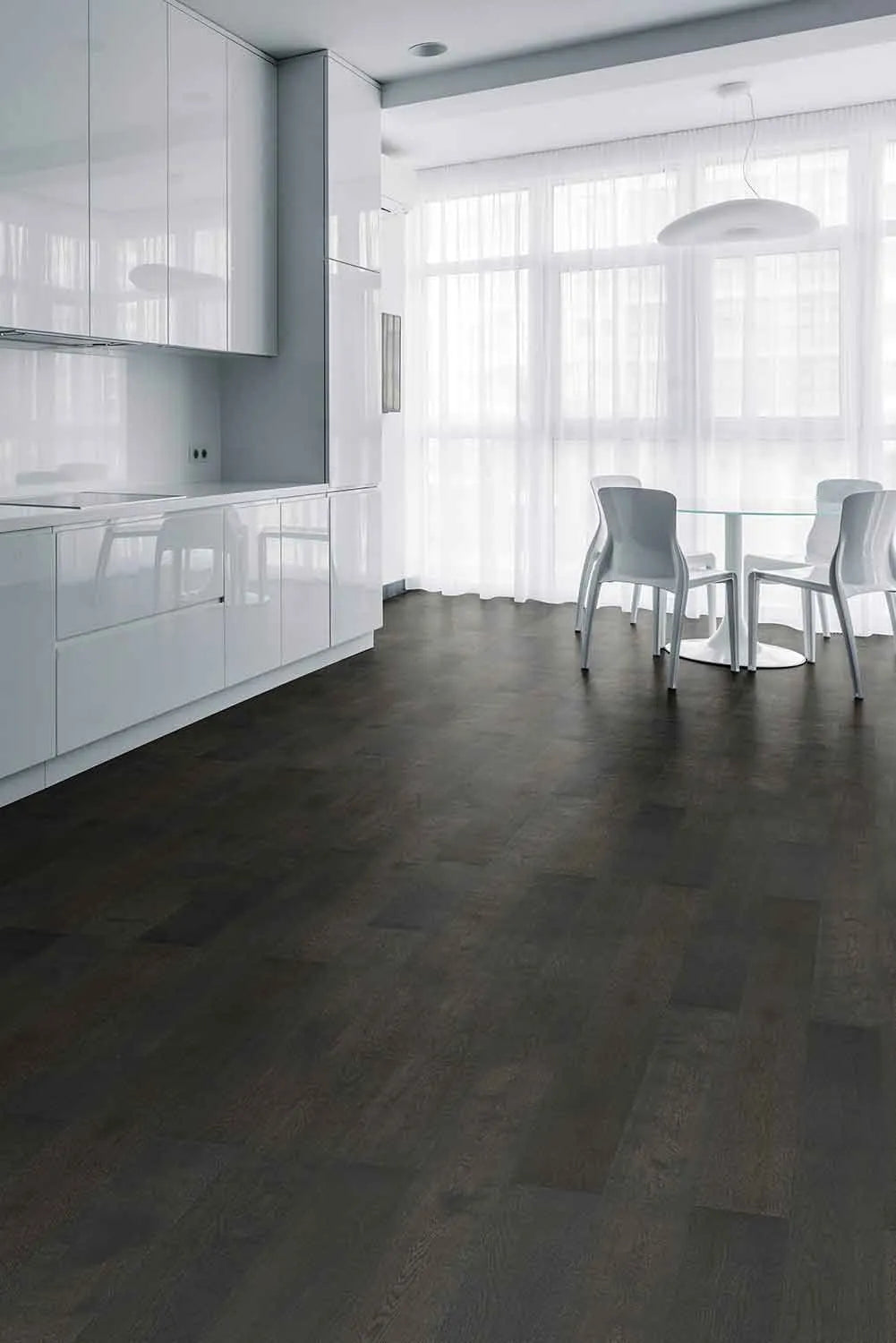 Midnight Grey iDesign Chevron Flooring 15/3mm installed in a modern open-plan kitchen-diner with glossy white cabinetry, glass dining table, and sheer curtains.