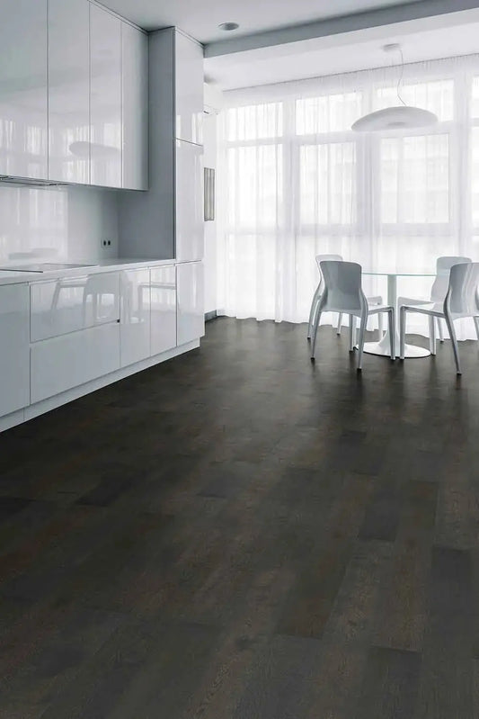 Midnight Grey iDesign15 Oak Flooring 15/3mm installed in a modern open-plan kitchen and dining area with white gloss cabinets, glass dining table, and sheer curtains.