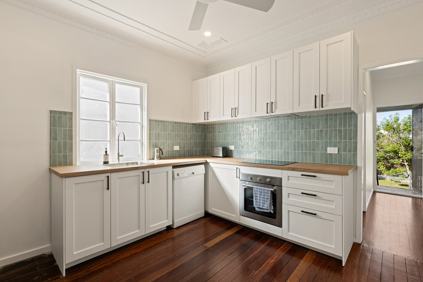 Mini Green Glossy 50x150mm tiles used as a kitchen splashback with white shaker cabinets, timber benchtops, and stainless steel oven.