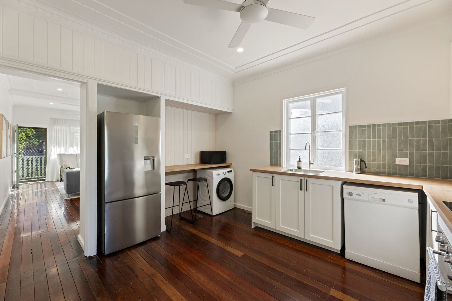 Mini Green Glossy 50x150mm tiles installed as a kitchen splashback behind a white shaker cabinet, timber benchtop, and window with natural light.