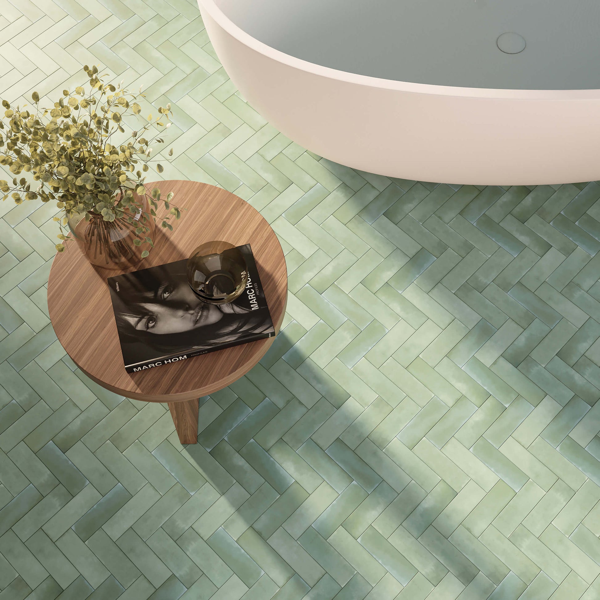 Mini Green Matt 50x150mm tiles laid in a herringbone pattern on a bathroom floor beside a freestanding white bathtub and wooden side table.