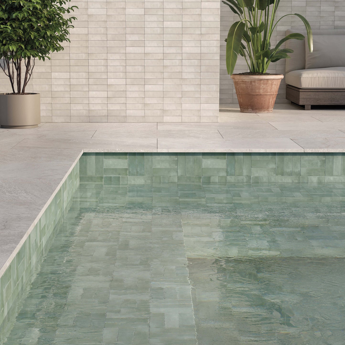 Mini Green Matt 50x150mm tiles lining a swimming pool interior and surround, paired with light stone coping, potted tropical plants, and a neutral outdoor seating area.