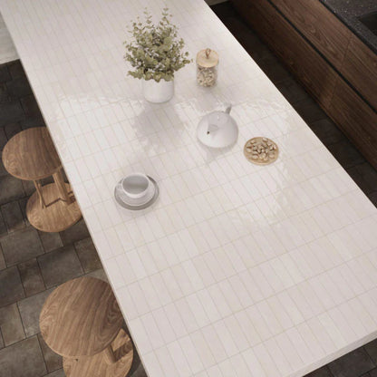 Overhead view of Mini Pure White Glossy 50x150mm tiles forming a sleek kitchen island countertop styled with wooden stools, a white teapot, and a potted plant.