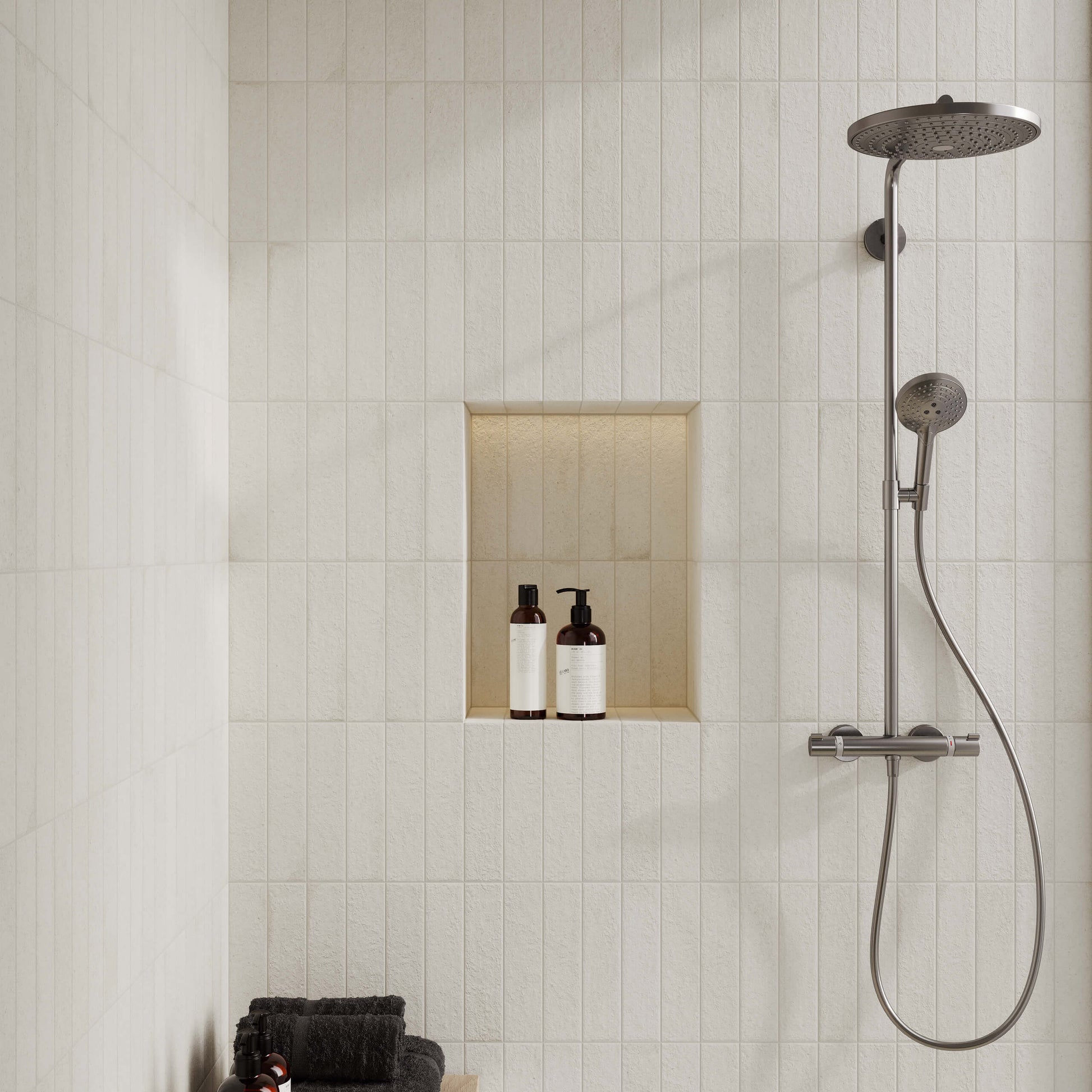 Miniature Fornace Bianco Minerale 60x240mm tiles installed vertically in a modern shower, featuring a built-in niche, brushed steel rain shower system, and dark folded towels.
