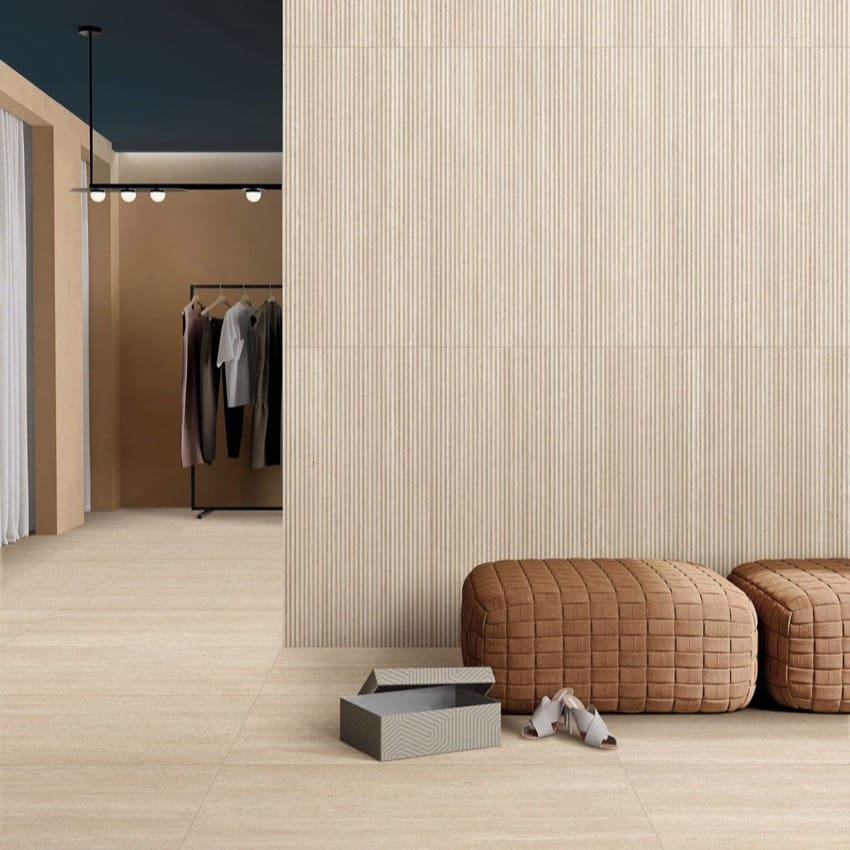 Tallow Bamboo Feature Travertine Look Beige 600x1200mm tiles installed as a textured ribbed feature wall in a modern boutique with tan quilted ottomans and a clothing rack.