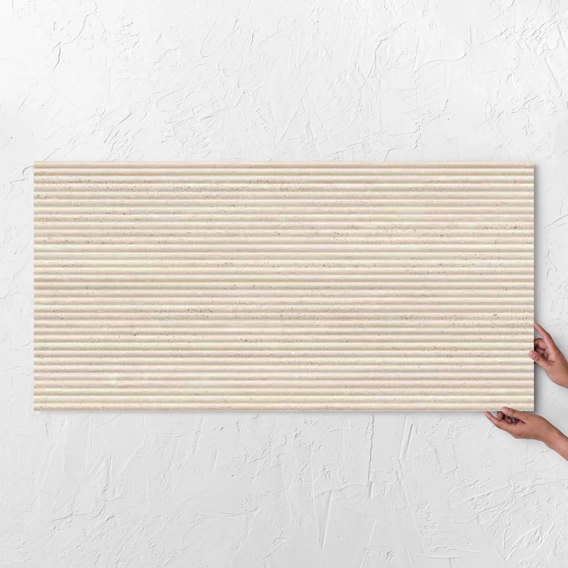 Hands holding a Tallow Bamboo Feature Travertine Look Ivory 600x1200mm tile against a white rendered wall, showing the tile surface