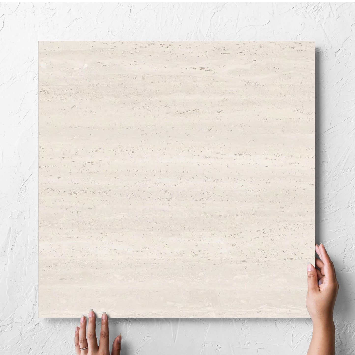Hand holding a single Tallow Vein Cut Travertine Look Ivory 600x600mm tile against a white rendered wall, showing the beige matt surface