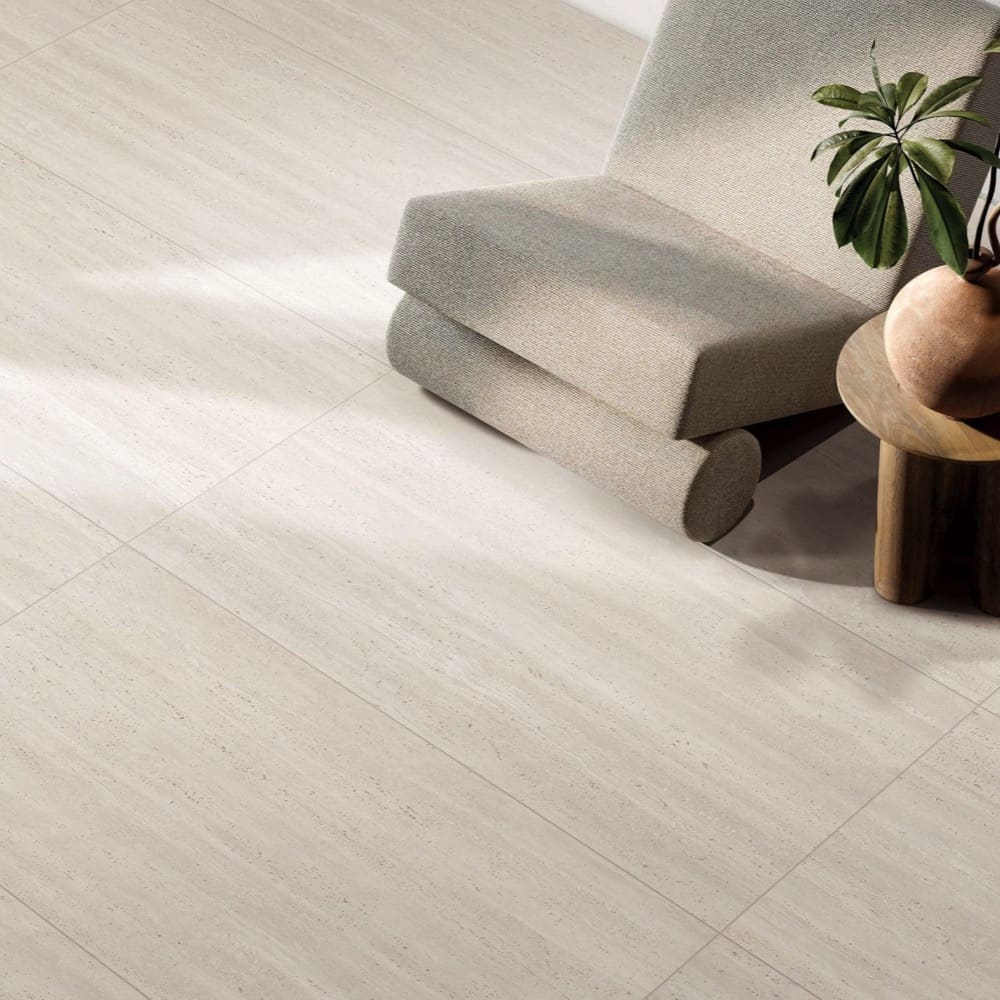 Tallow Vein Cut Travertine Look Ivory 600x600mm cream travertine-look floor tiles styled in a modern living room with a linen lounge chair and timber side table.
