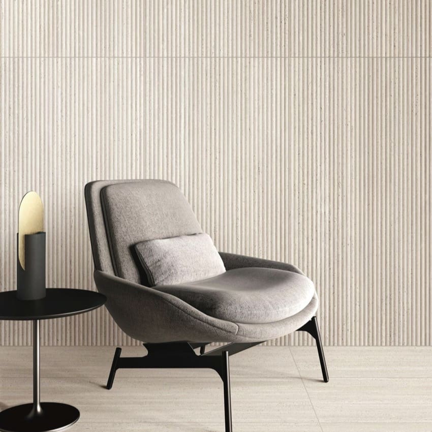Tallow Vein Cut Travertine Look Ivory 600x600mm tiles installed as a ribbed feature wall behind a contemporary grey armchair and black side table.