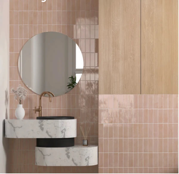 Miyako Crystal Pink Gloss 50x150mm tiles covering a modern bathroom wall paired with a marble floating vanity, round mirror, and brass faucet.