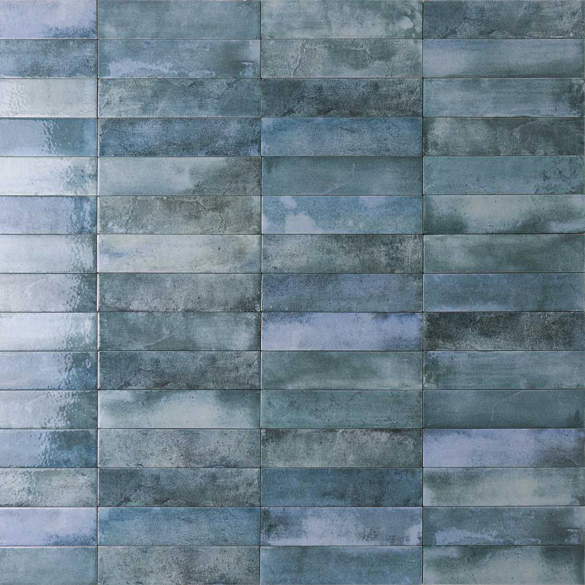 Close-up of Mojave Denim Brick 60x250mm wall tiles arranged in a staggered brick pattern with a glossy, variegated blue-teal glaze finish.