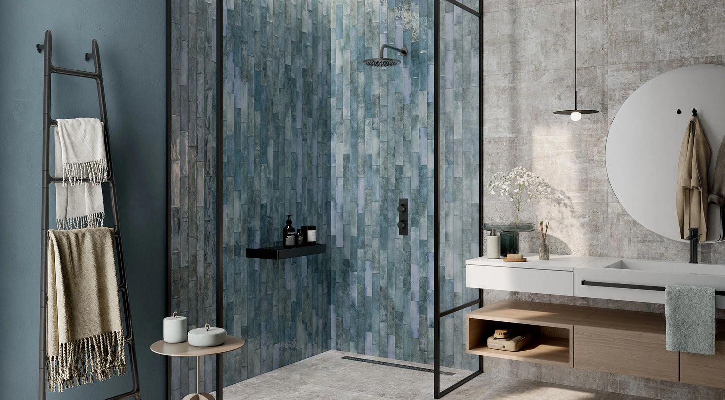 Mojave Denim Brick 60x250mm tiles covering a walk-in shower feature wall in blue-grey tones, paired with a floating white vanity and black fixtures.