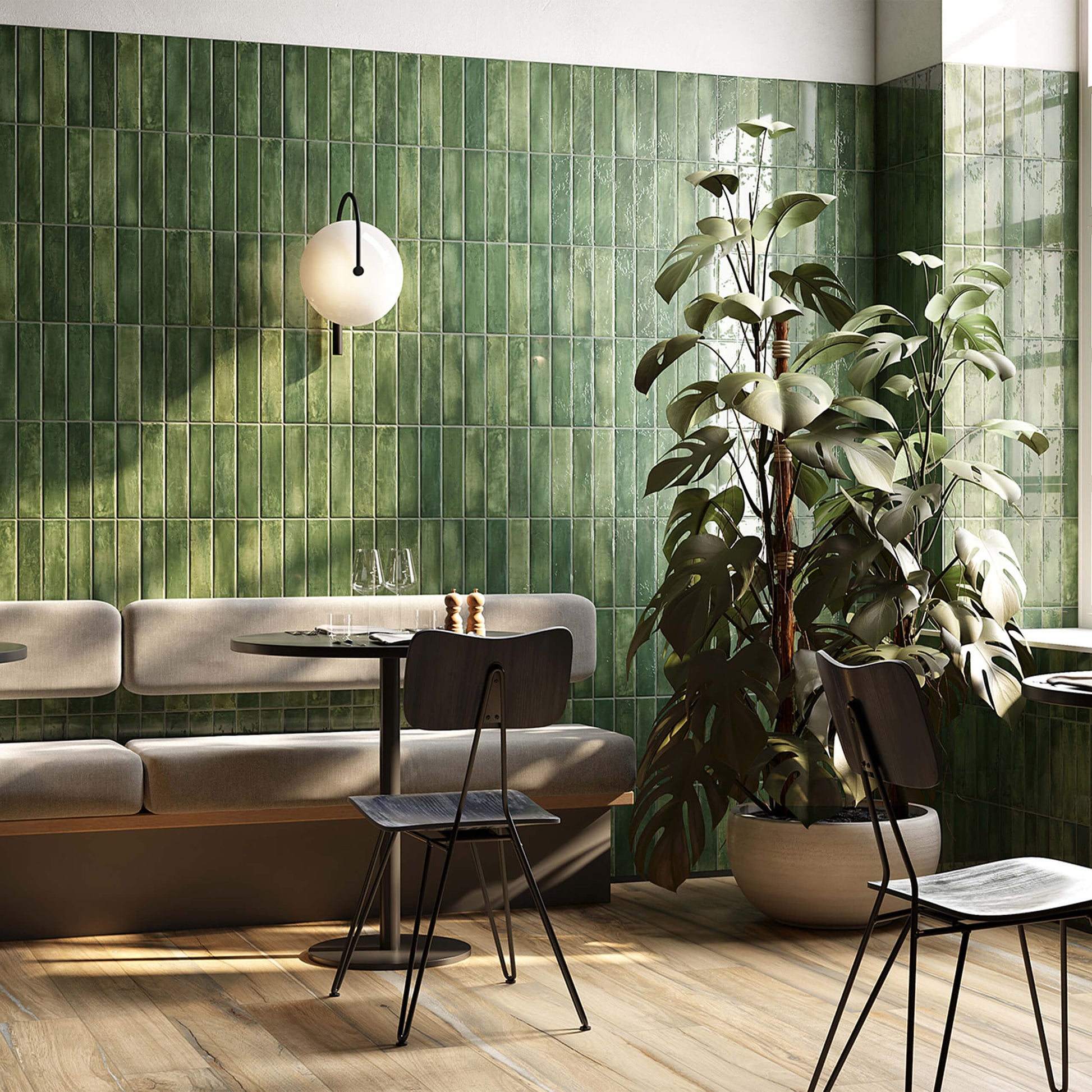 Mojave Green Brick 60x250mm glossy green vertical stack tiles covering a full restaurant wall behind a grey banquette seat, round table, and large monstera plant.