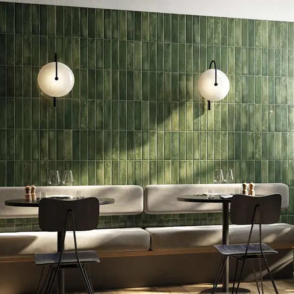 Mojave Green Brick 60x250mm tiles covering a full restaurant wall in deep glazed green, paired with a curved banquette, bistro tables, and globe wall sconces.