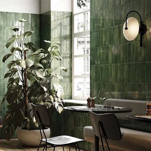 Mojave Green Brick 60x250mm glazed tiles covering a restaurant dining area wall, styled with a large potted plant, round marble table, and black arc wall sconce.