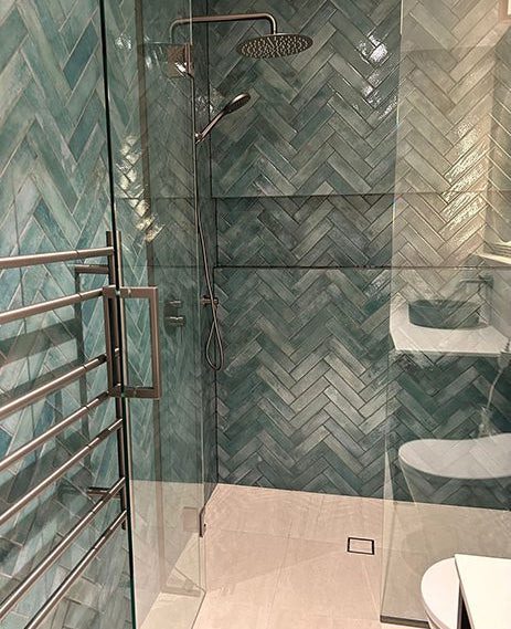 Mojave Sea Water Brick 60x250mm tiles laid in a herringbone pattern covering the walls of a modern walk-in shower enclosure with rainfall showerhead and heated towel rail.