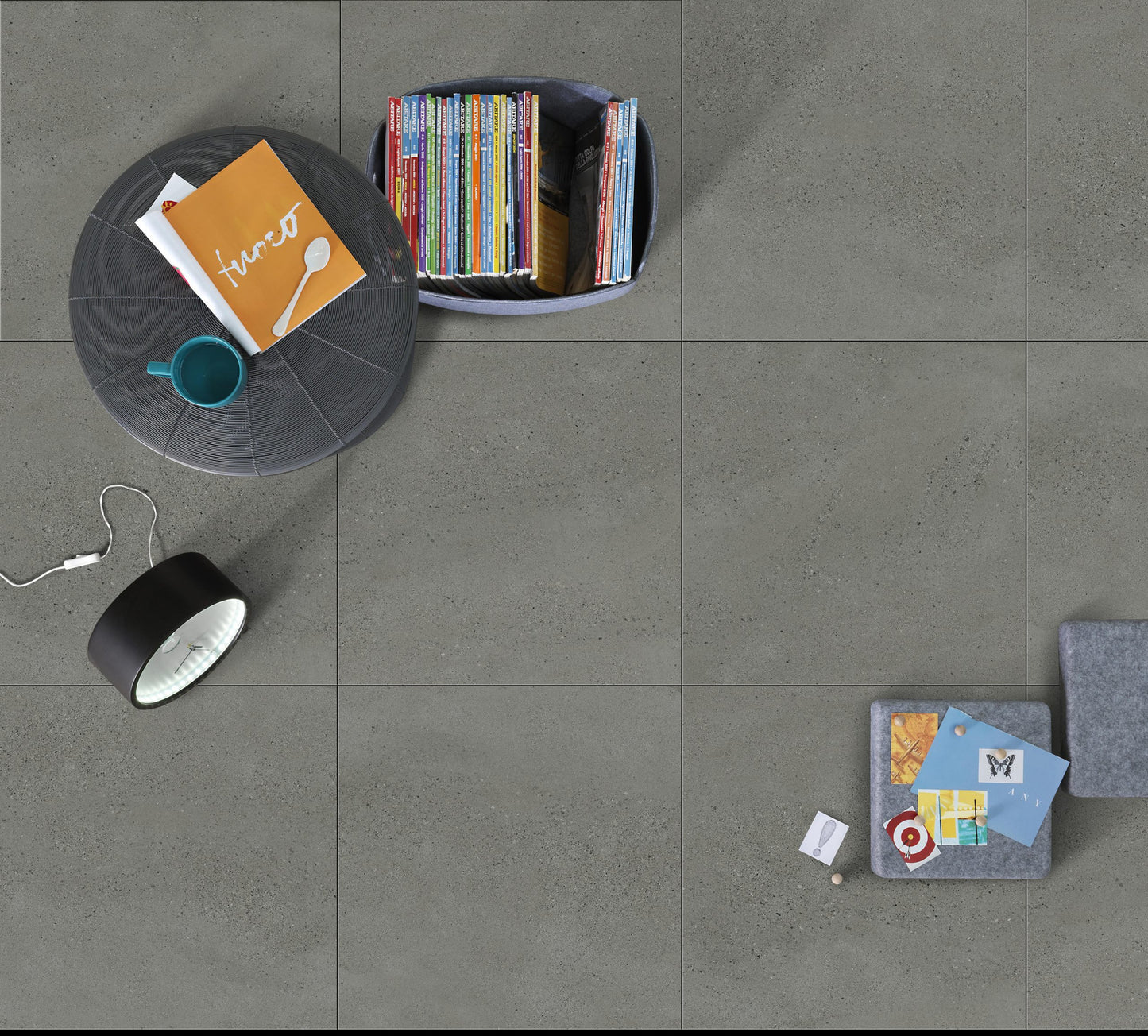 Moonstone Oyster Matte 300x600mm grey concrete-look floor tiles styled overhead with a round coffee table, books, and a desk lamp.