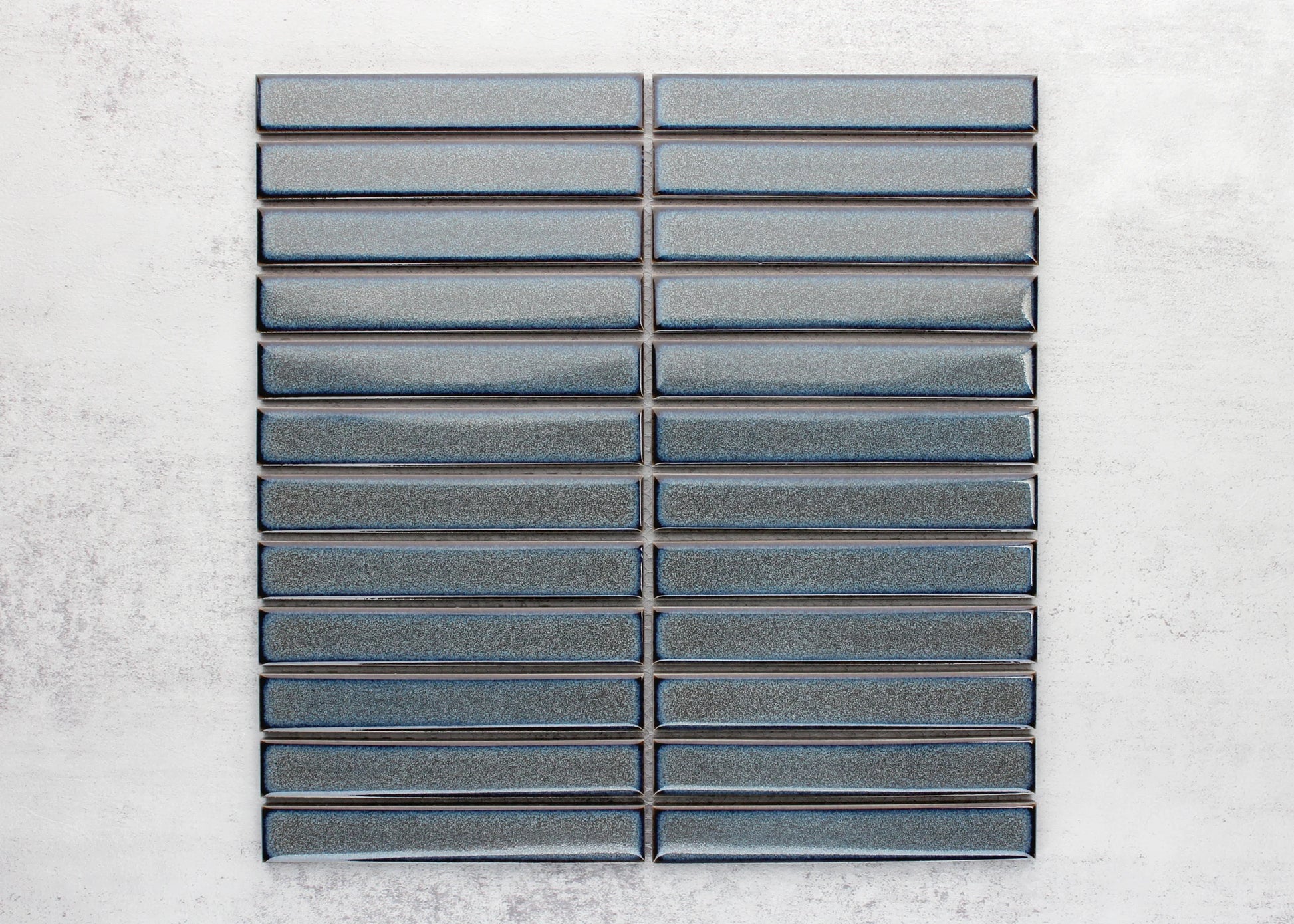 Flat lay pack shot of Mottled Grey Gloss KitKat Straight Bone Pattern 22x145mm tiles arranged in stacked rows showing glossy blue-grey finish and bevelled edges.