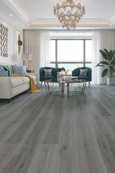 Mystic Grey Urban Laminate 12mm Flooring 12mm installed in a modern living room featuring teal accent chairs, a gold chandelier, and floor-to-ceiling sheer curtains.