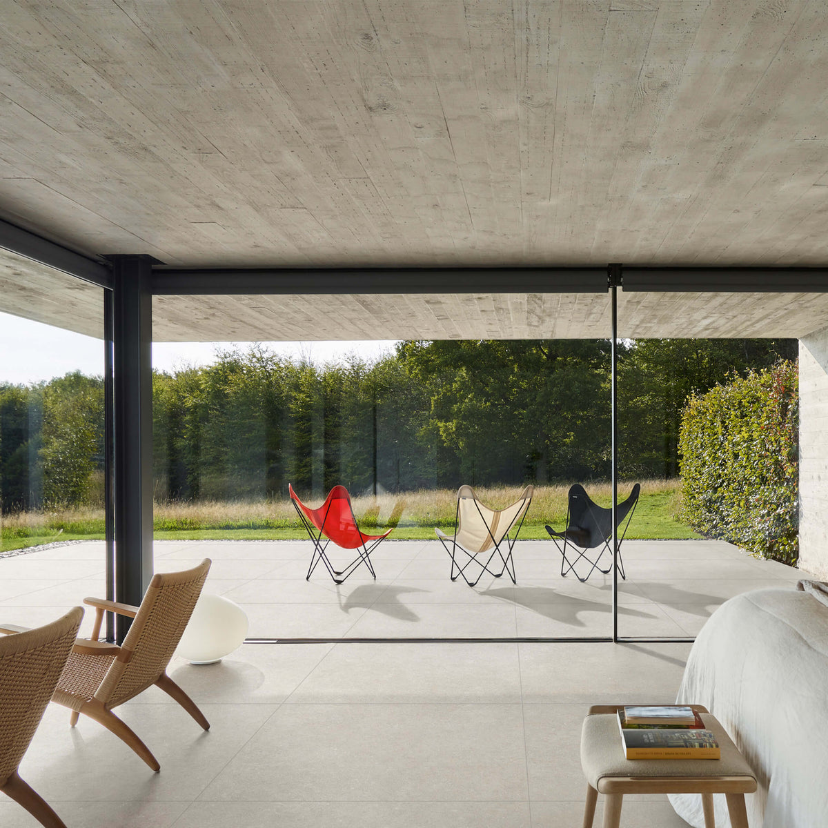 Mystone Berici Bianco Naturale 600x600mm large-format white tiles laid across an open-plan living room and outdoor patio, with butterfly chairs and floor-to-ceiling glazing.