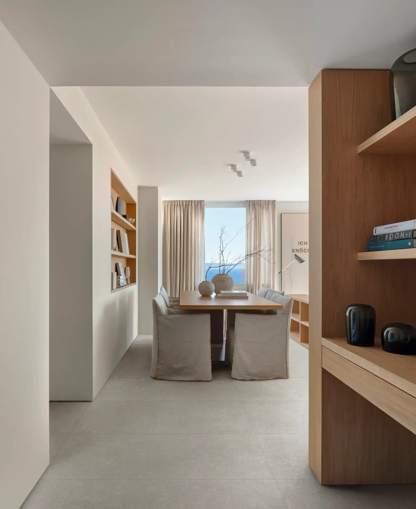 Mystone Berici Grigio Naturale 600x1200mm tiles laid on a dining room floor with linen chairs, wooden shelving, and a large ocean-view window.