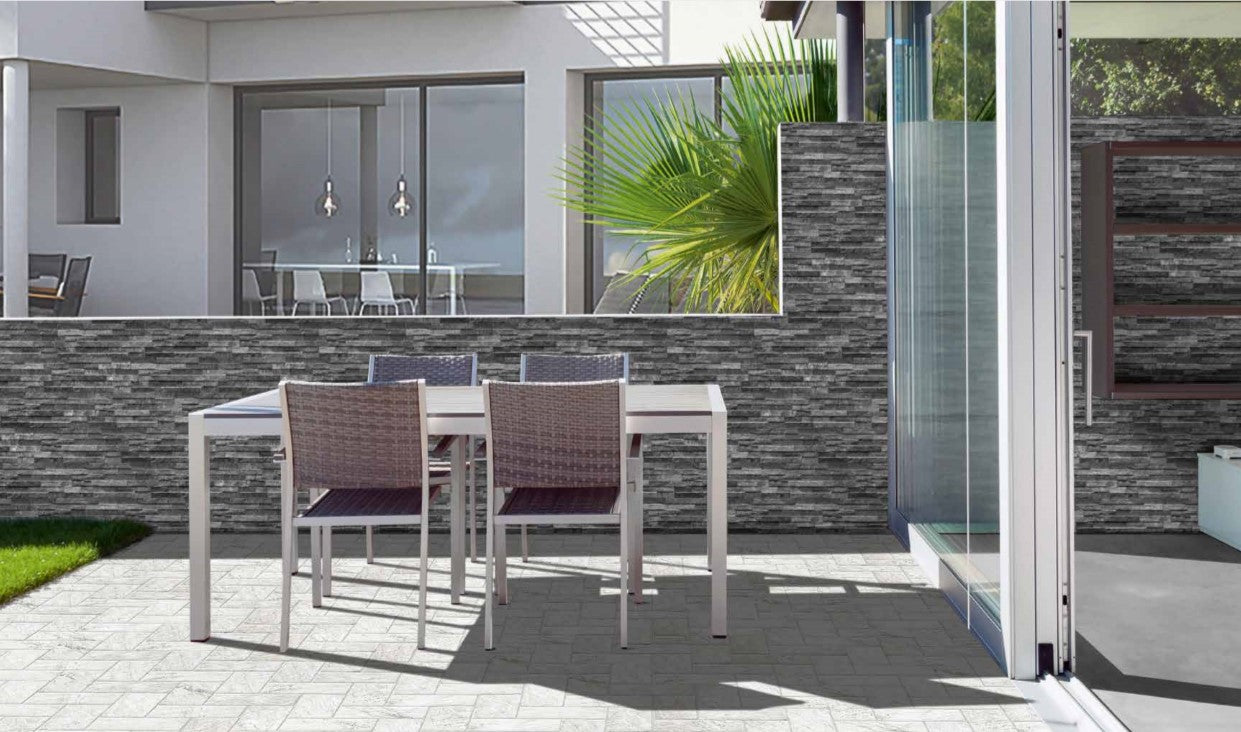 Natura Lava 160X400mm dark grey stacked stone feature wall tiles installed on an outdoor patio with wicker dining furniture and sliding glass doors.