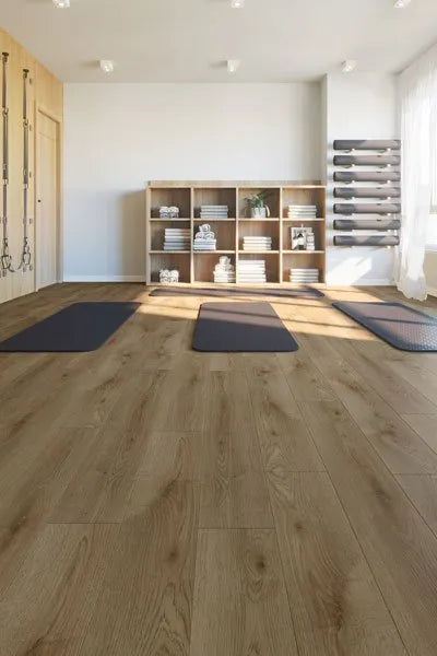 Natural Oak Urban Laminate 12mm Flooring 12mm installed in a bright yoga studio with dark exercise mats and wooden shelving unit.