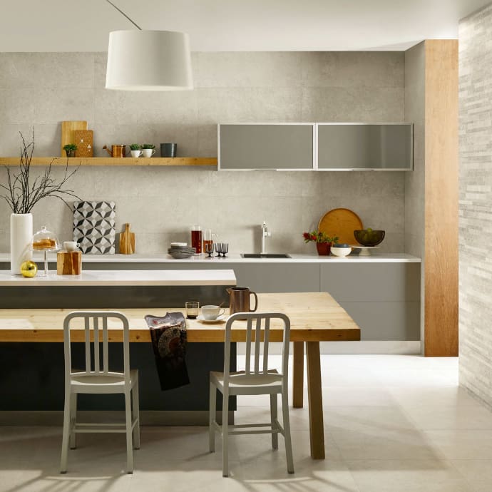 Nest Grey Floor Tile 610x610mm laid in a modern open-plan kitchen-diner featuring a wooden dining table, grey cabinetry, and a large white pendant light.