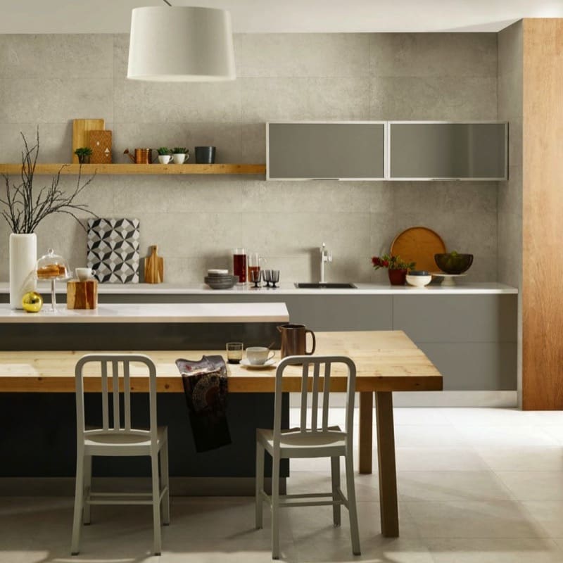 Nest White 610x610mm large-format tiles covering a modern kitchen wall behind grey cabinetry, open shelving, and a natural wood dining table.