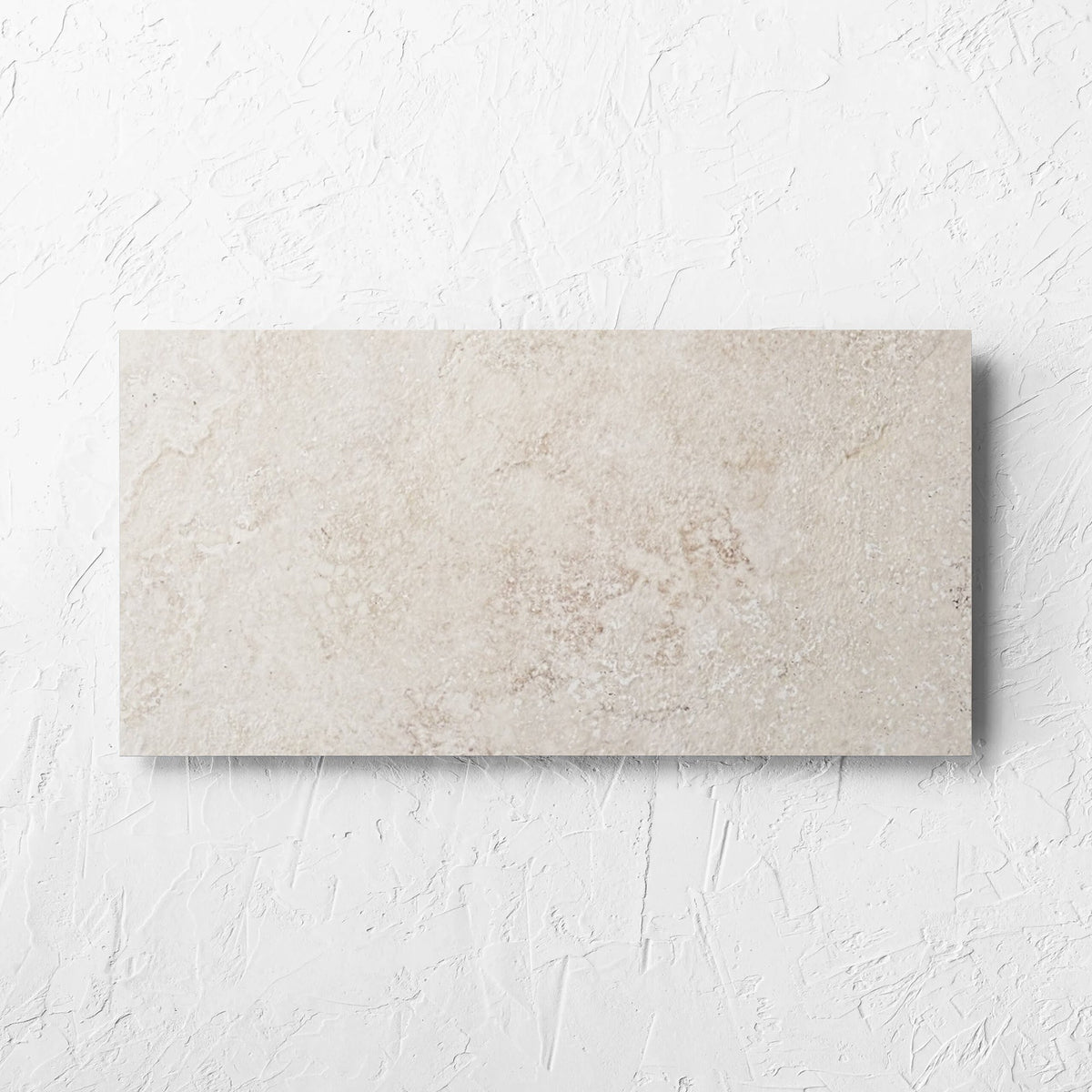 Norcia Travertine Beige 300x600mm tile laid flat on a white rendered wall, showing the beige travertine surface