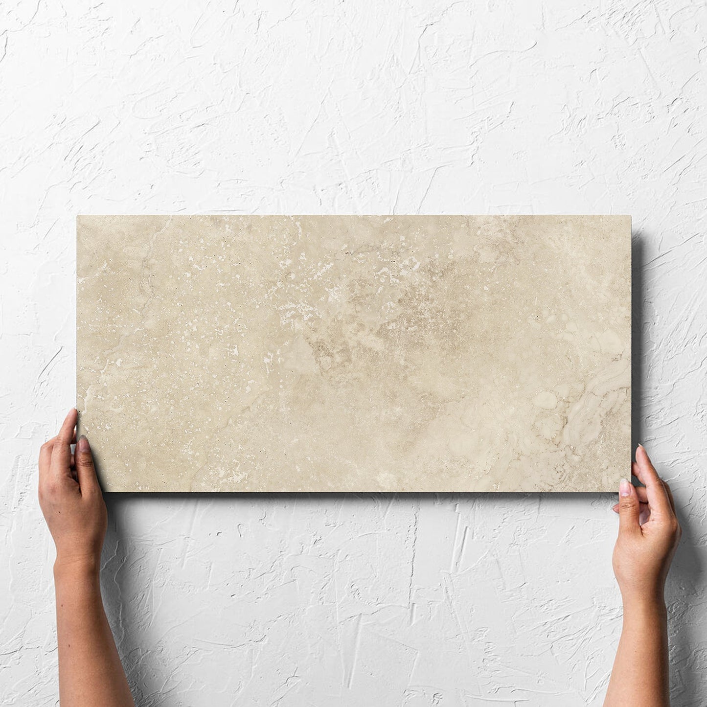 Hand holding a single Norcia Travertine Beige 300x600mm tile against a white rendered wall, showing the beige matt surface