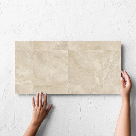 Hand holding a single Norcia Travertine Beige Decor 300x600mm tile against a white rendered wall, showing the tile surface