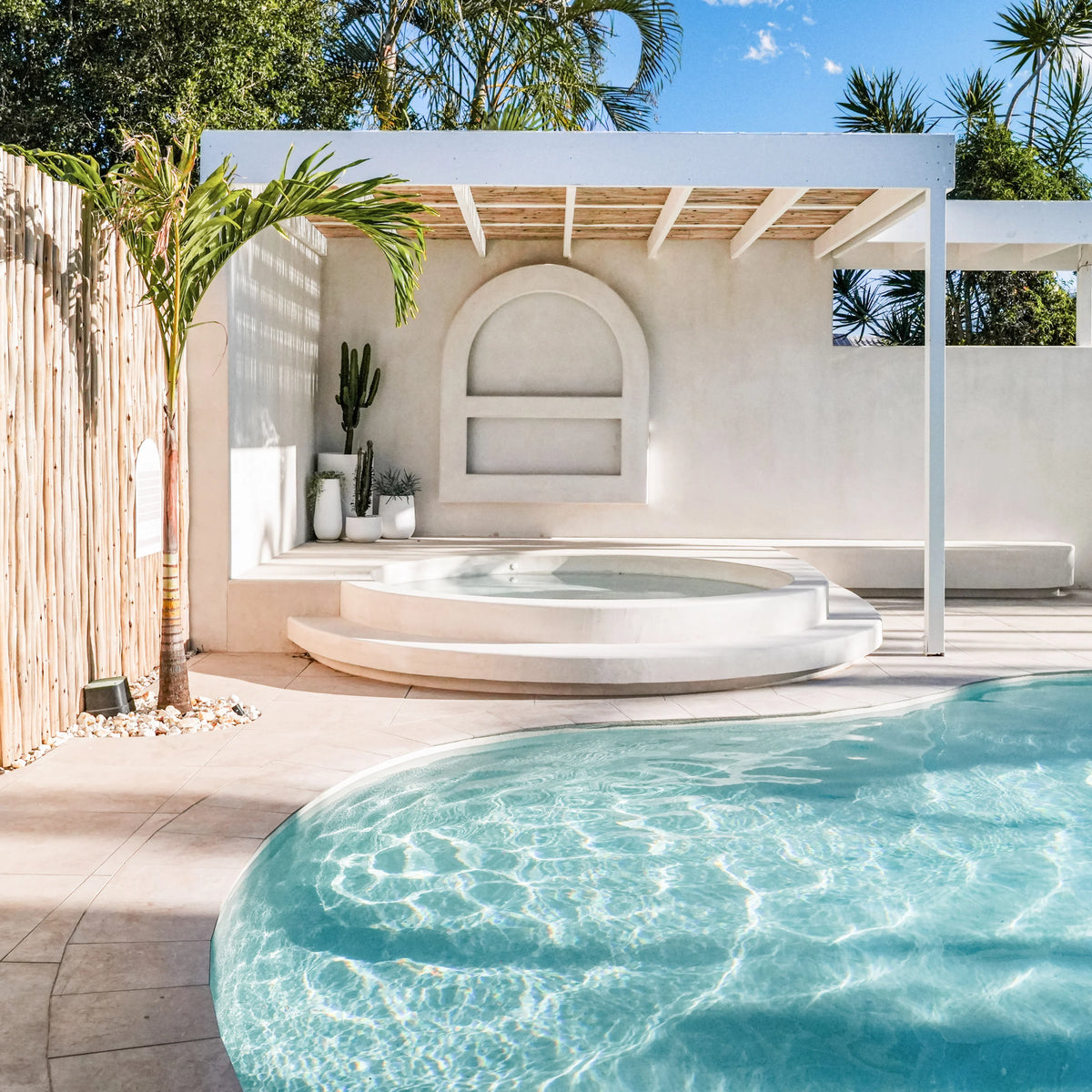 Norcia Travertine Beige External Rectified Paver 600x600x20mm installed around a resort-style outdoor pool and circular spa with white render walls and timber pergola.