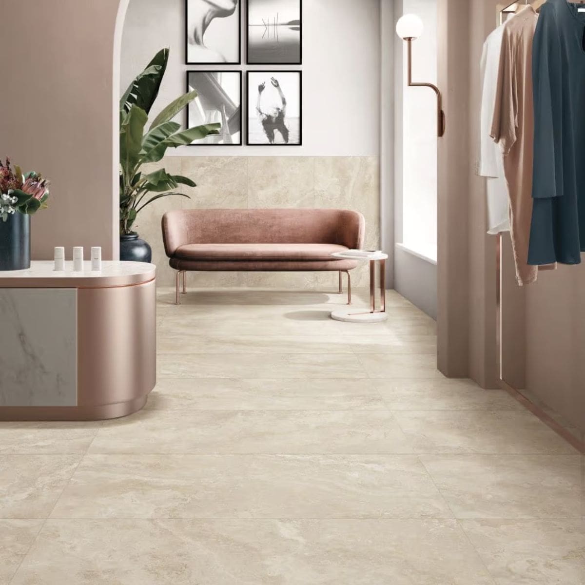 Norcia Travertine Beige Honed 600x1200mm tiles laid across a chic boutique retail floor featuring a blush velvet sofa, rose gold reception desk, and clothing rack.