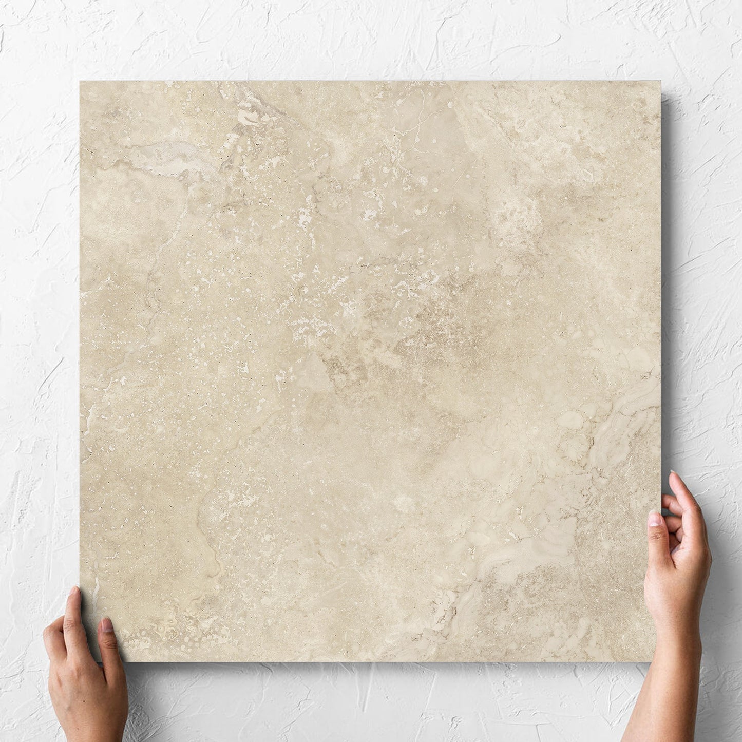 Hand holding a single Norcia Travertine Beige Honed 600x600mm tile against a white rendered wall, showing the tile surface