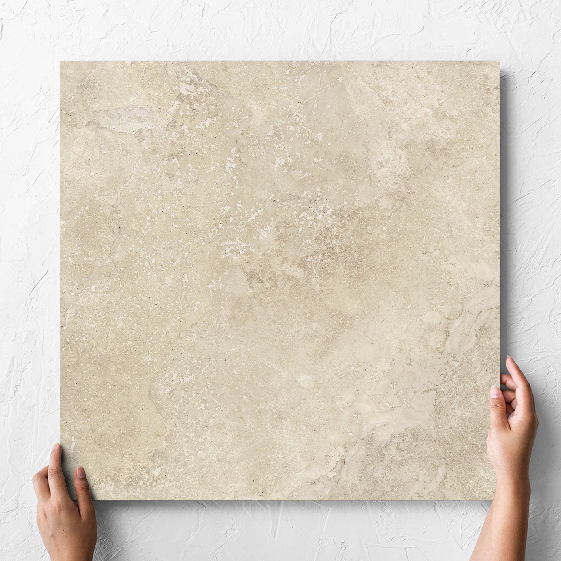 Hand holding a single Norcia Travertine Beige Honed 600x600mm tile against a white rendered wall, showing the tile surface