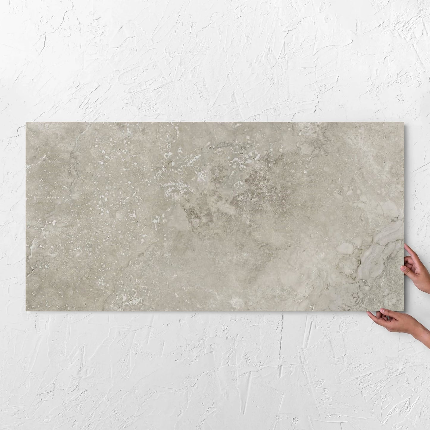 Hands holding a Norcia Travertine Grey Bamboo Feature 600x1200mm tile against a white rendered wall, showing the tile surface