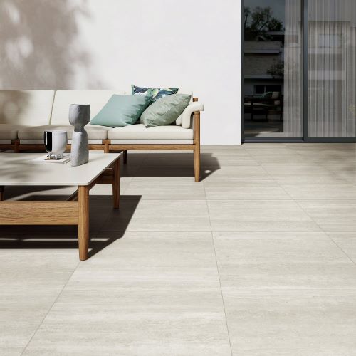 Norcia Travertine Light Decor 300x600mm tiles laid on a sunlit outdoor patio featuring a timber-framed sofa and low coffee table.