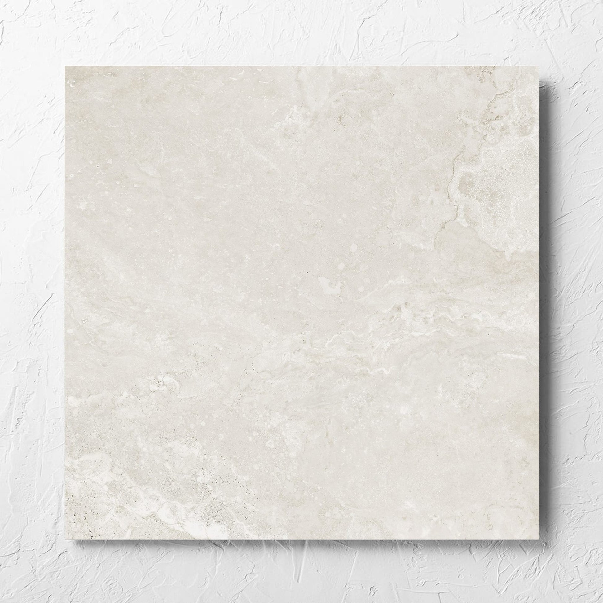Norcia Travertine Light Honed 600x600mm tile laid flat on a white rendered wall, showing the tile surface