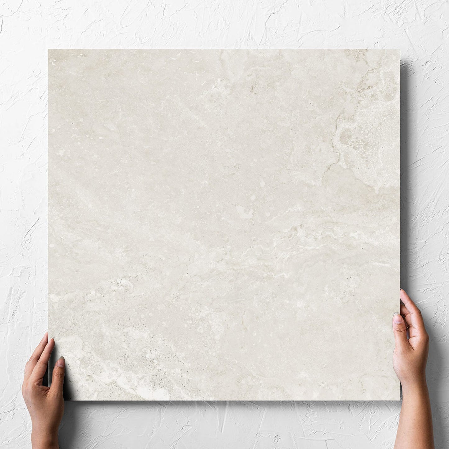 Hand holding a single Norcia Travertine Light Honed 600x600mm tile against a white rendered wall, showing the tile surface