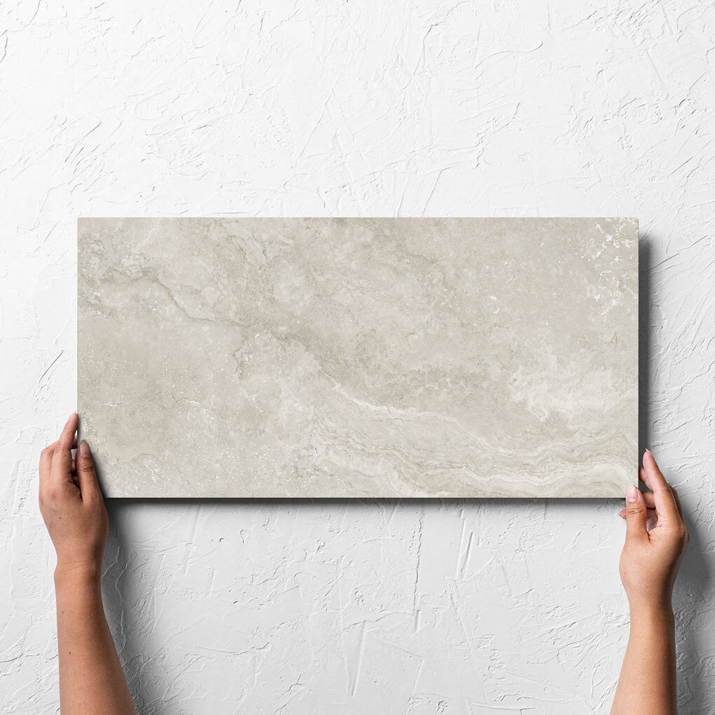 Hand holding a single Norcia Travertine Silver Decor 300x600mm tile against a white rendered wall, showing the tile surface