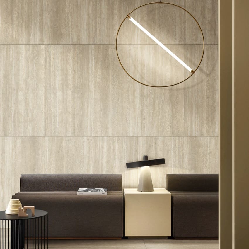 Norcia Vein Cut Beige tiles as a floor-to-ceiling feature wall behind a modern sofa and brass pendant light